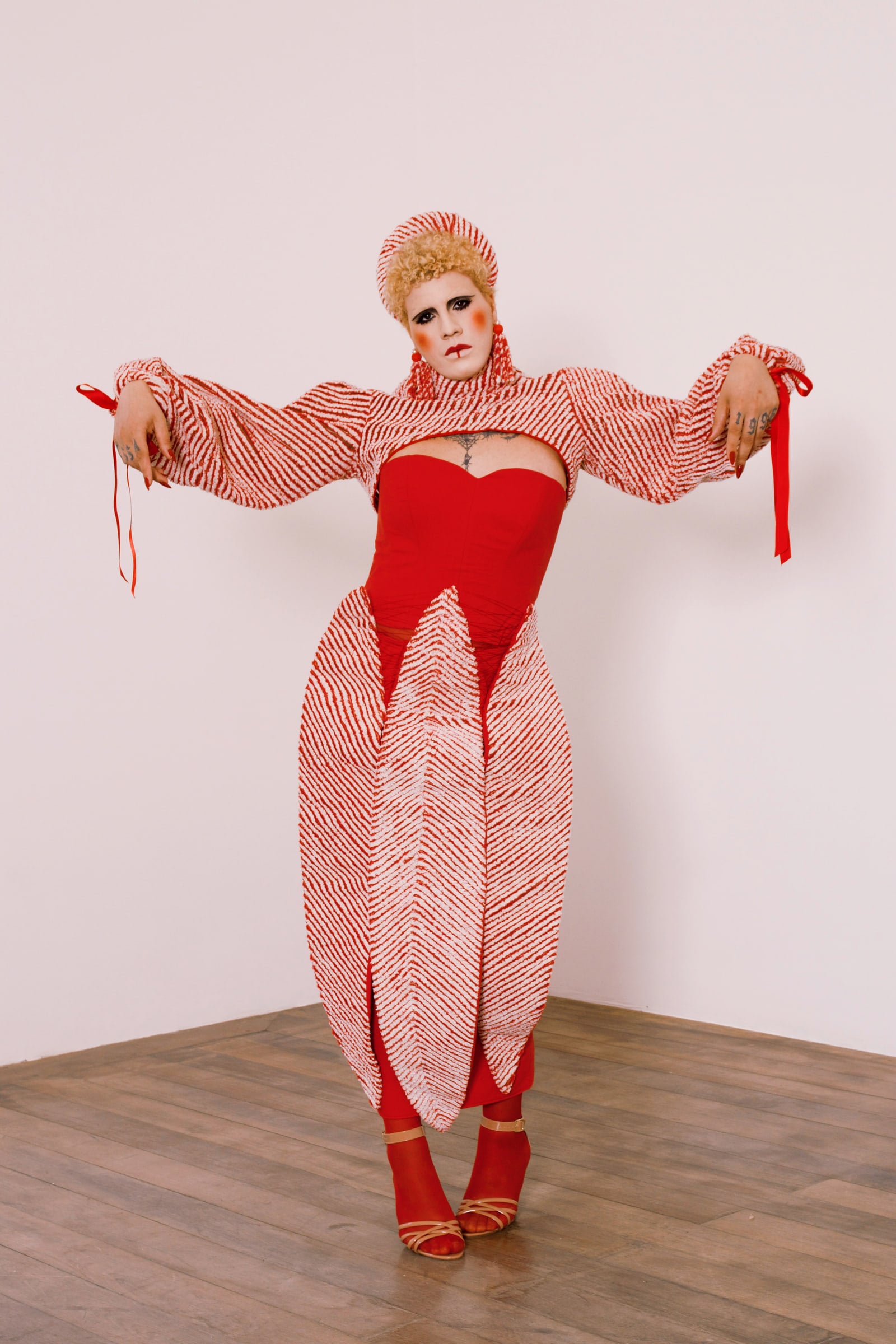 Full-length photograph of the look: a fitted red dress, wide sleeves and long panels of red-and-white striped fabric.
